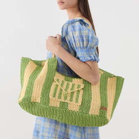 Model carrying Damson Madder Apple Stripe paper tote bag with green and yellow stripes and logo detail, short top handles. Model wears blue check