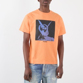 Model wearing Pleasures orange cotton T-shirt with blue and grey graphic print, styled with distressed light-wash jeans.