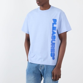 Model wearing Pleasures Buzzed Logo T-Shirt in sky blue with vertical blue logo print, styled with light wash jeans.