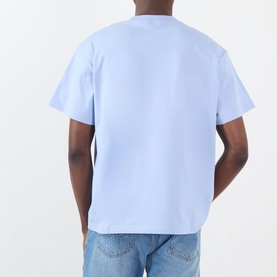 Model wearing Pleasures Buzzed Logo T-Shirt in Sky, rear view, relaxed fit with dropped shoulders, styled with light blue jeans.