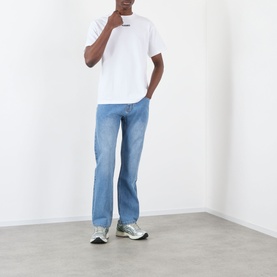 Model wearing Pleasures white cotton T-shirt with light blue straight-leg jeans and grey chunky trainers