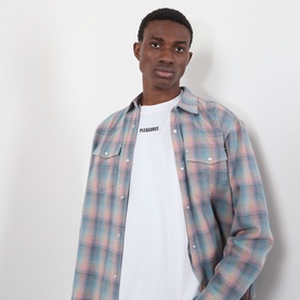 Model wearing Pleasures white cotton T-shirt, styled with a blue and pink plaid overshirt