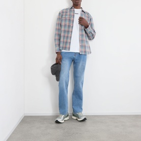 Model wearing Pleasures white cotton T-shirt, styled with blue plaid overshirt, light-wash jeans, and grey trainers.