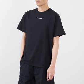 Model wearing Pleasures black cotton T-shirt with small chest logo, styled with black track pants.