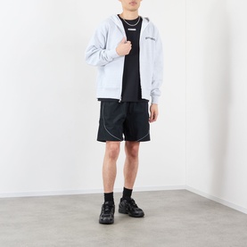 Model wearing Pleasures black T-shirt, styled with grey zip-up hoodie, black shorts, and chunky black trainers.