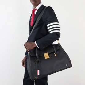 Model carrying Thom Browne Mr. Thom Soft Leather Holdall in black with gold-tone hardware, worn with navy four-bar blazer and red tie.
