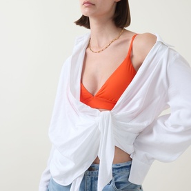 Model wearing Lauren Triangle Bikini Top in Sunburst Orange with V-neckline and narrow straps, styled with white shirt and gold necklace