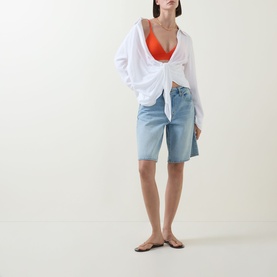 Model wearing Lauren Triangle Bikini Top in Sunburst Orange with white oversized shirt, light-wash denim shorts and flat sandals.