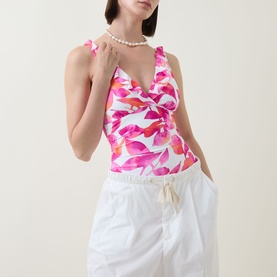 Model wearing Lauren swimsuit in multi floral pink print with ruched V-neckline and ruffle straps, styled with white wide-leg trousers