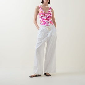 Model wearing Lauren multi floral print swimsuit with ruched detail, styled with white wide-leg trousers and black sandals.
