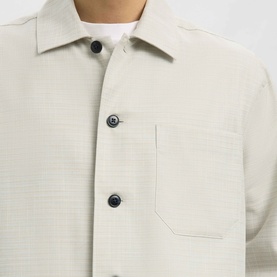 Model wearing Selected Casual Shirt in White Pepper, close-up of textured fabric, dark navy buttons and chest pocket detail