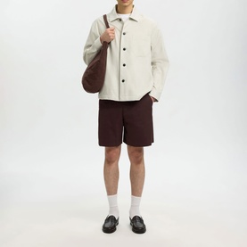 Model wearing Selected White Pepper casual shirt with dark burgundy shorts, white socks and black loafers, carrying brown shoulder bag.