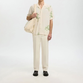 Model wearing Selected Egret casual shirt with green floral print, styled with matching cream trousers, tote bag and black loafers