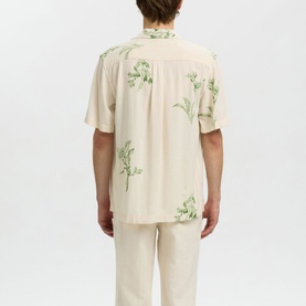Model wearing Selected Casual Shirt in Egret, short-sleeve with green floral print, shown from the back, styled with matching trousers.