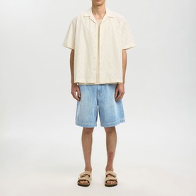 Model wearing Selected Light Blue Denim shorts, styled with a cream short-sleeve shirt and tan sandals