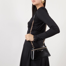Model carrying Givenchy Antigona Vanity Crossbody Bag in black smooth leather, gold-tone chain strap, styled with black long-sleeve top and skirt