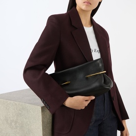 Model carrying Givenchy Pinch Soft Leather Clutch in black lambskin with gold-tone hardware, styled with a burgundy blazer.