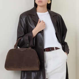 Model carrying Givenchy Antigona East-West Bowling Bag in Ebony Brown suede, gold-tone hardware, top handle. Styled with dark leather coat.