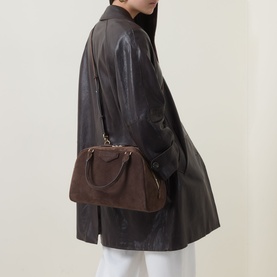 Model carrying Givenchy Antigona East-West Bowling Bag in Ebony Brown suede, gold-tone hardware, worn cross-body over black leather jacket.