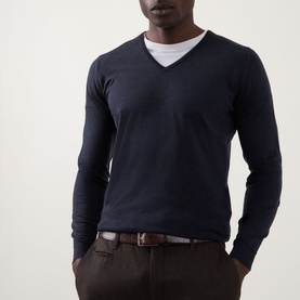 Model wearing John Smedley Blenheim Extra Fine Knit Sweater in Hepburn smoke, V-neck wool knit, styled with white tee and brown trousers.