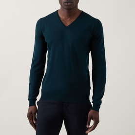 Model wearing John Smedley Blenheim Extra Fine Knit Sweater in Richardson green, V-neckline, long sleeves, ribbed trims, styled with navy trousers.
