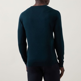 Model wearing John Smedley Blenheim Extra Fine Knit Sweater in Richardson green, rear view, V-neck, long sleeves, ribbed trims, paired with navy