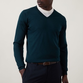 Model wearing John Smedley Blenheim Extra Fine Knit Sweater in Richardson green, V-neck, styled with white tee and navy trousers.