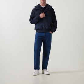 Model wearing Calvin Klein Jeans Mixed Media Logo Windbreaker in Dark Sapphire, styled with blue jeans and white trainers.