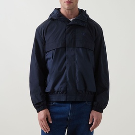 Model wearing Calvin Klein Jeans Mixed Media Logo Windbreaker in Dark Sapphire, hooded zip-front jacket with chest pockets, styled with blue jeans.