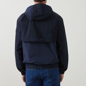 Model wearing Calvin Klein Jeans Mixed Media Logo Windbreaker in Dark Sapphire, rear view showing hood, embroidered logo, and blue jeans.