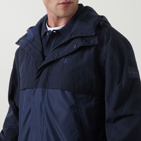 Model wearing Calvin Klein Jeans Mixed Media Logo Windbreaker in Dark Sapphire, hooded, with embroidered logo and mixed-media panels.