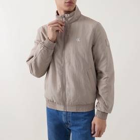 Model wearing Calvin Klein Jeans Harrington Logo Weatherproof Jacket in Vintage Khaki, zip fastening, elasticated waistband, styled with blue jeans.