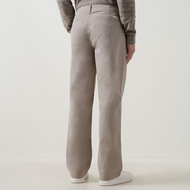 Model wearing Calvin Klein Jeans 90S Straight-Leg Chinos in Vintage Khaki, rear view, styled with a grey knit top and white trainers.