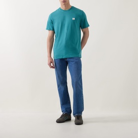 Model wearing Calvin Klein Jeans Logo Badge 30s Classic T-Shirt in North Sea teal, styled with blue jeans and dark trainers.