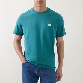 Model wearing Calvin Klein Jeans Logo Badge 30s Classic T-Shirt in North Sea teal, short sleeves, crew neck, small logo badge, styled with blue jeans.