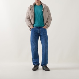 Model wearing Calvin Klein Jeans Logo Badge 30s Classic T-Shirt in North Sea, styled with beige zip jacket, blue jeans and grey trainers.