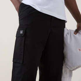 Model wearing Calvin Klein Jeans Twill Cargo Trousers in black, showing logo badge and cargo pocket detail, styled with a white tee.