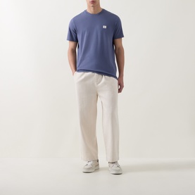 Model wearing Calvin Klein Jeans Logo Badge 30s Classic T-Shirt in Blue Nomad, styled with cream trousers and white trainers.