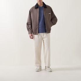 Model wearing Calvin Klein Jeans Logo Badge 30s Classic T-Shirt in Blue Nomad, styled with brown zip jacket, cream trousers and white trainers.
