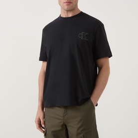 Model wearing Calvin Klein Jeans Monogram Logo T-Shirt in black, crew neck, short sleeves, with tonal chest logo. Styled with khaki cargo trousers.