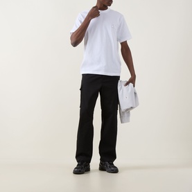 Model wearing Calvin Klein Jeans Monogram Logo T-Shirt in Bright White, styled with black cargo trousers and chunky trainers.