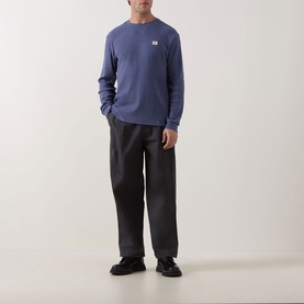 Model wearing Calvin Klein Jeans Waffle Knit Logo T-Shirt in Blue Nomad, long sleeves, chest logo badge, styled with dark trousers and black trainers.