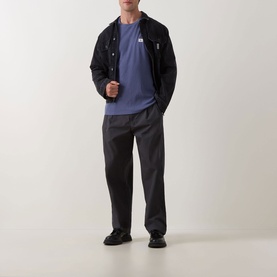 Model wearing Calvin Klein Jeans Waffle Knit Logo T-Shirt in Blue Nomad, styled with black zip jacket, dark grey trousers and black shoes.