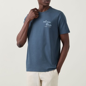 Model wearing Calvin Klein Jeans Travel Line Logo T-Shirt in Dark Slate, crew neck with chest script logo, styled with cream trousers.