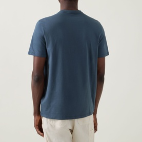 Model wearing Calvin Klein Jeans Travel Line Logo T-Shirt in Dark Slate, back view, crew neck, short sleeves, paired with cream trousers