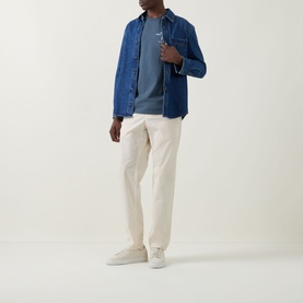 Model wearing Calvin Klein Jeans Travel Line Logo T-Shirt in Dark Slate, styled with blue overshirt, cream trousers and white trainers.