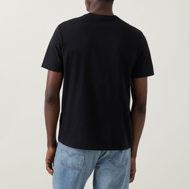 Model wearing Calvin Klein Jeans Travel Line Logo T-Shirt in black, rear view, short sleeves, straight hem, styled with light blue jeans.