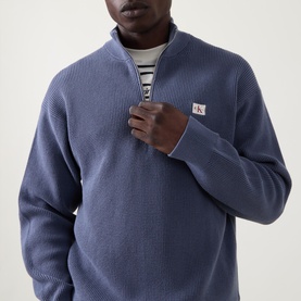 Model wearing Calvin Klein Jeans Waffle-Knit Logo Half-Zip Sweatshirt in Blue Nomad, styled with a striped crew-neck top underneath.