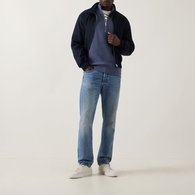 Model wearing Calvin Klein Jeans Waffle-Knit Logo Half-Zip Sweatshirt in Blue Nomad, styled with navy jacket, blue jeans and white trainers.
