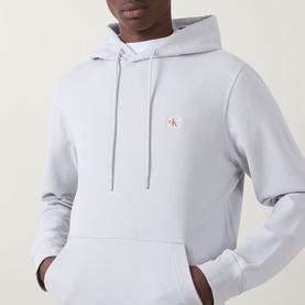 Model wearing Calvin Klein Jeans Monogram Badge Drawstring Hoodie in Marble Grey with kangaroo pocket and small logo badge at chest